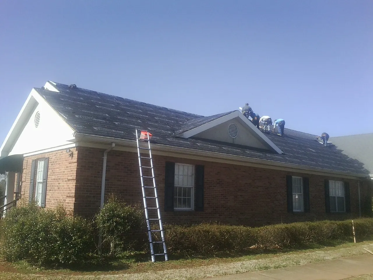 Crew tearing shingles off a brick ranch roof with a ladder set — Emergency Roof Repair work by our crew in Grottoes