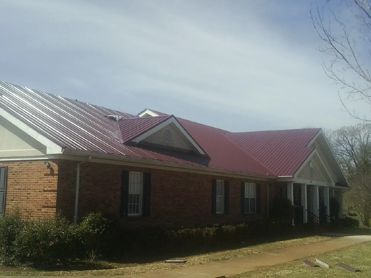 Red metal roof with gabled entries on a long brick building, from a Hail Damage Roof Repair job in Grottoes