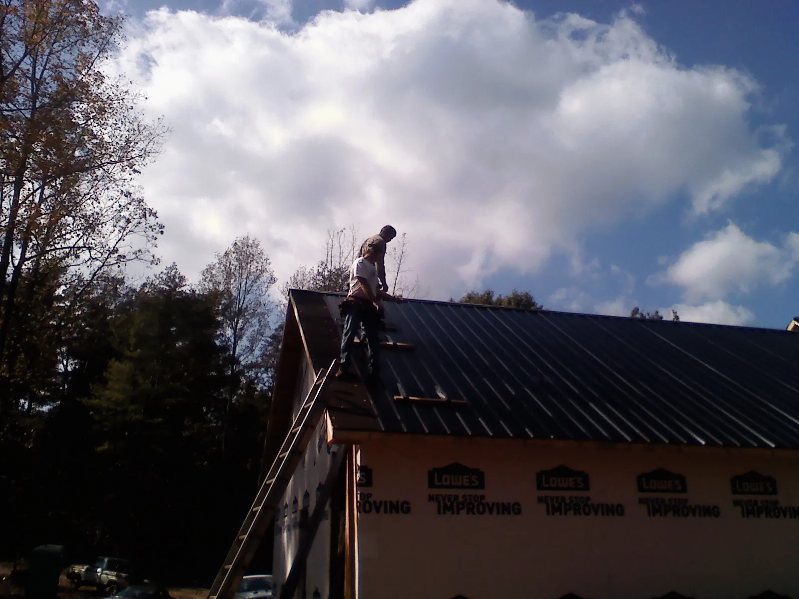 Roofer fastening dark metal panels high against a cloudy sky, from a Roof Inspection job in Grottoes
