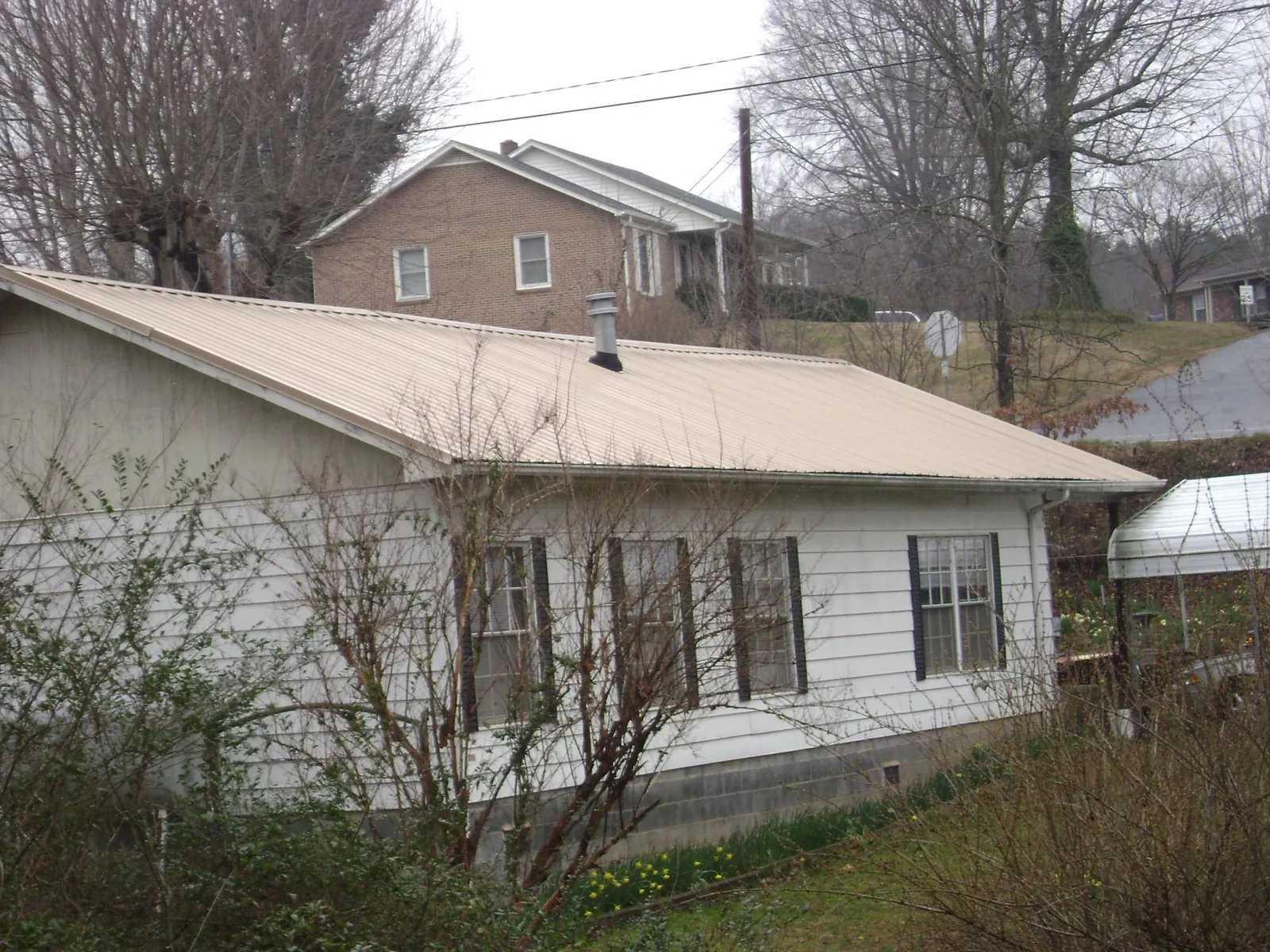 Tan metal roof on a white sided house set into a hillside — Commercial Roofing by Roofing Brothers in Grottoes